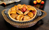 Handwoven round pie dish holder with handles displaying a baked apple pie in a glass dish.