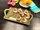 Gold tray with pastries on a wooden table with flowers and oranges.