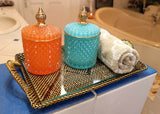 Two decorative jars, one orange and one blue, on a tray with a towel in a bathroom setting.