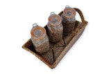 Three glass jars with wooden lids on a woven tray against a white background