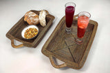 Two handwoven trays with handles, with bread, a bowl of nuts, and two glasses of juice on a white background
