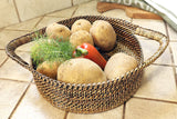 Wicker basket with potatoes, a red pepper, and dill on a tiled floor.