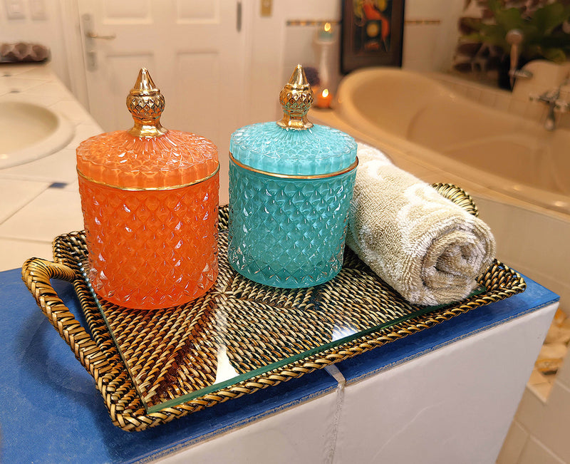 Two decorative jars, one orange and one blue, on a tray with a towel in a bathroom setting.